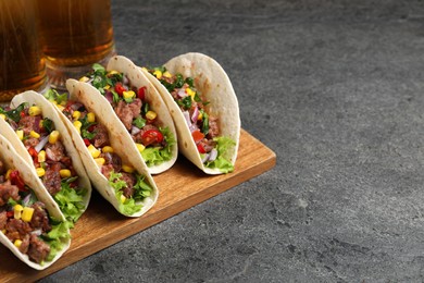 Photo of Delicious tacos with meat and vegetables on gray textured table, space for text