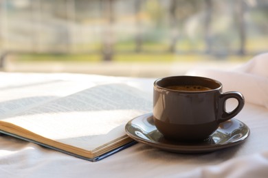 Photo of Aromatic morning coffee and open book on bed indoors