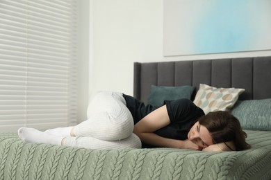 Sad young woman lying on bed at home