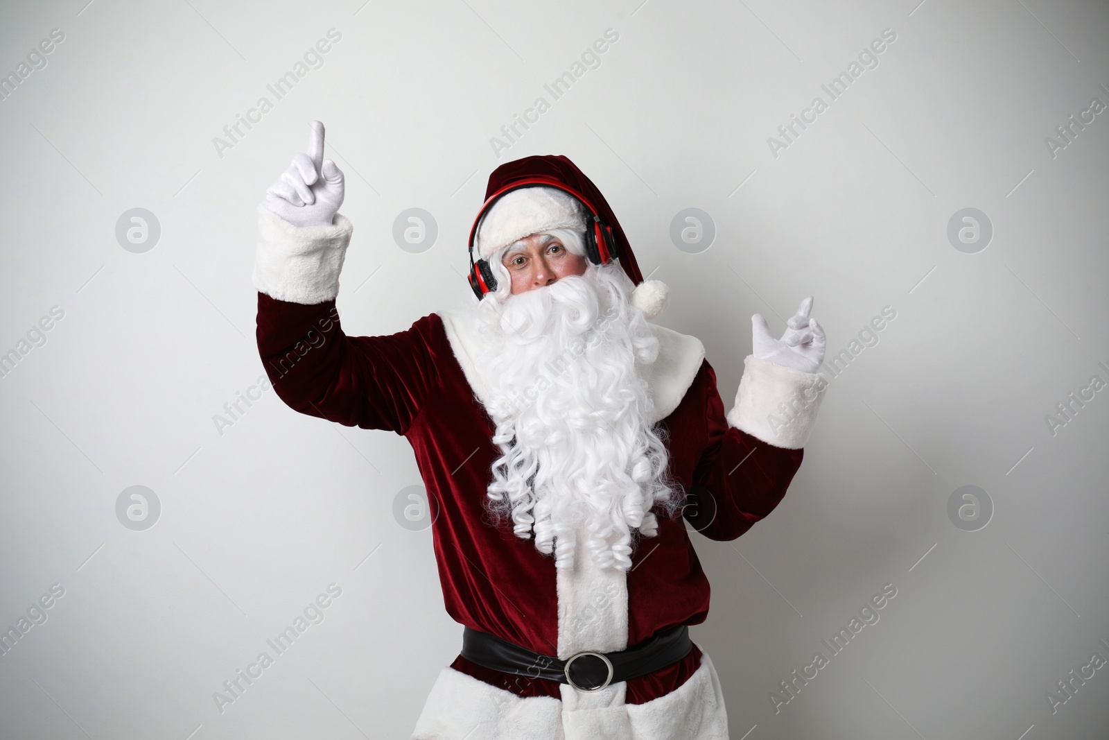 Photo of Santa Claus with headphones listening to Christmas music on light background