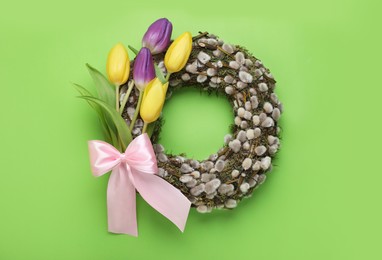 Photo of Wreath made of beautiful willow, colorful tulip flowers and pink bow on green background, top view