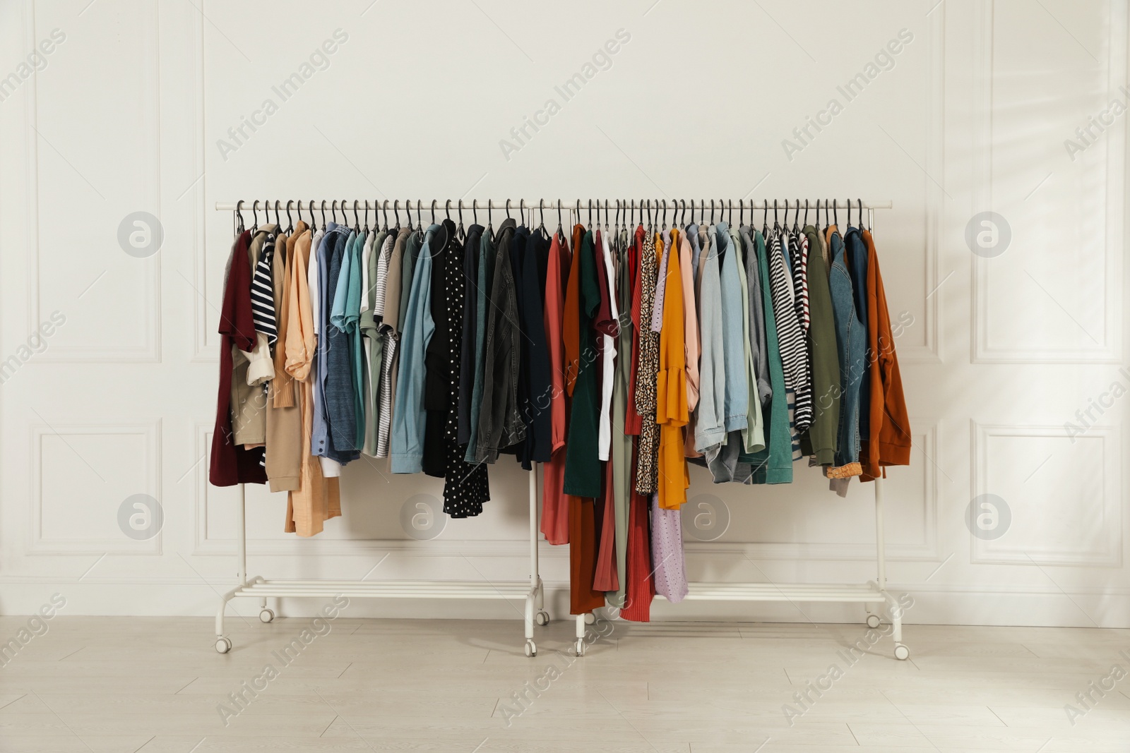 Photo of Racks with stylish clothes near white wall indoors. Fast fashion