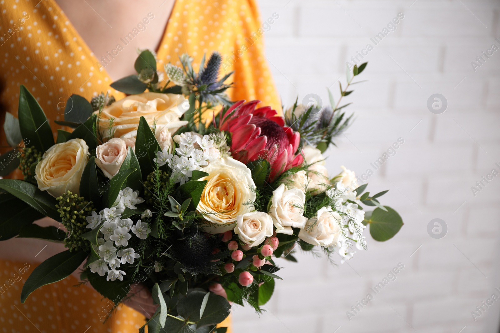 Photo of Woman with bouquet of beautiful roses near white brick wall, closeup