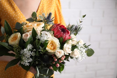 Photo of Woman with bouquet of beautiful roses near white brick wall, closeup