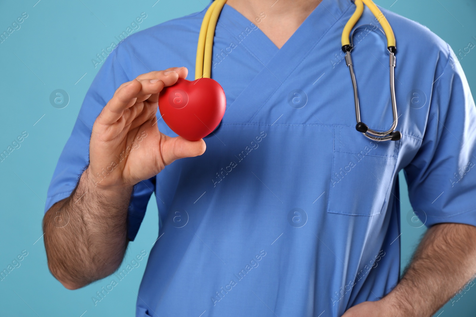 Photo of Doctor with stethoscope and red heart on light blue background, closeup. Cardiology concept