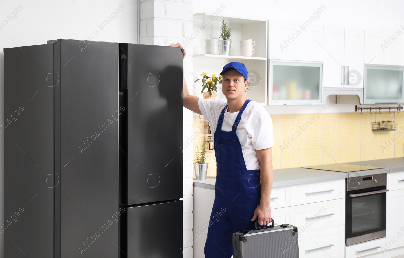 Photo of Male technician with tool box near refrigerator in kitchen