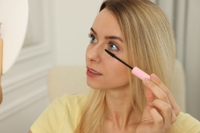Photo of Beautiful woman applying mascara with brush indoors, closeup