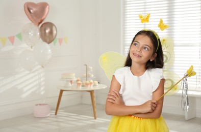 Photo of Cute little girl wearing fairy costume with wings and magic wand in decorated room. Space for text
