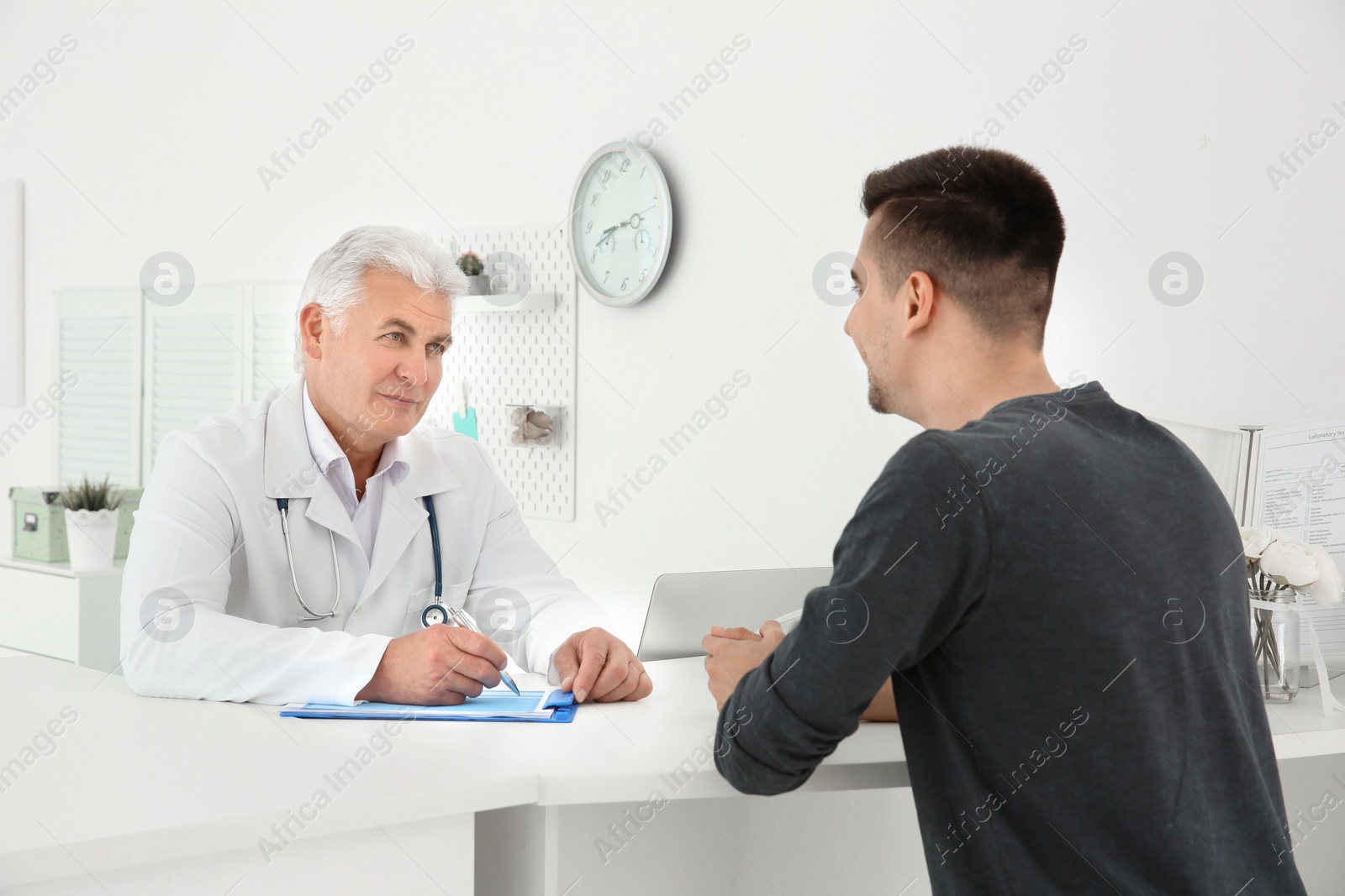 Photo of Senior male doctor working with client at reception desk in hospital