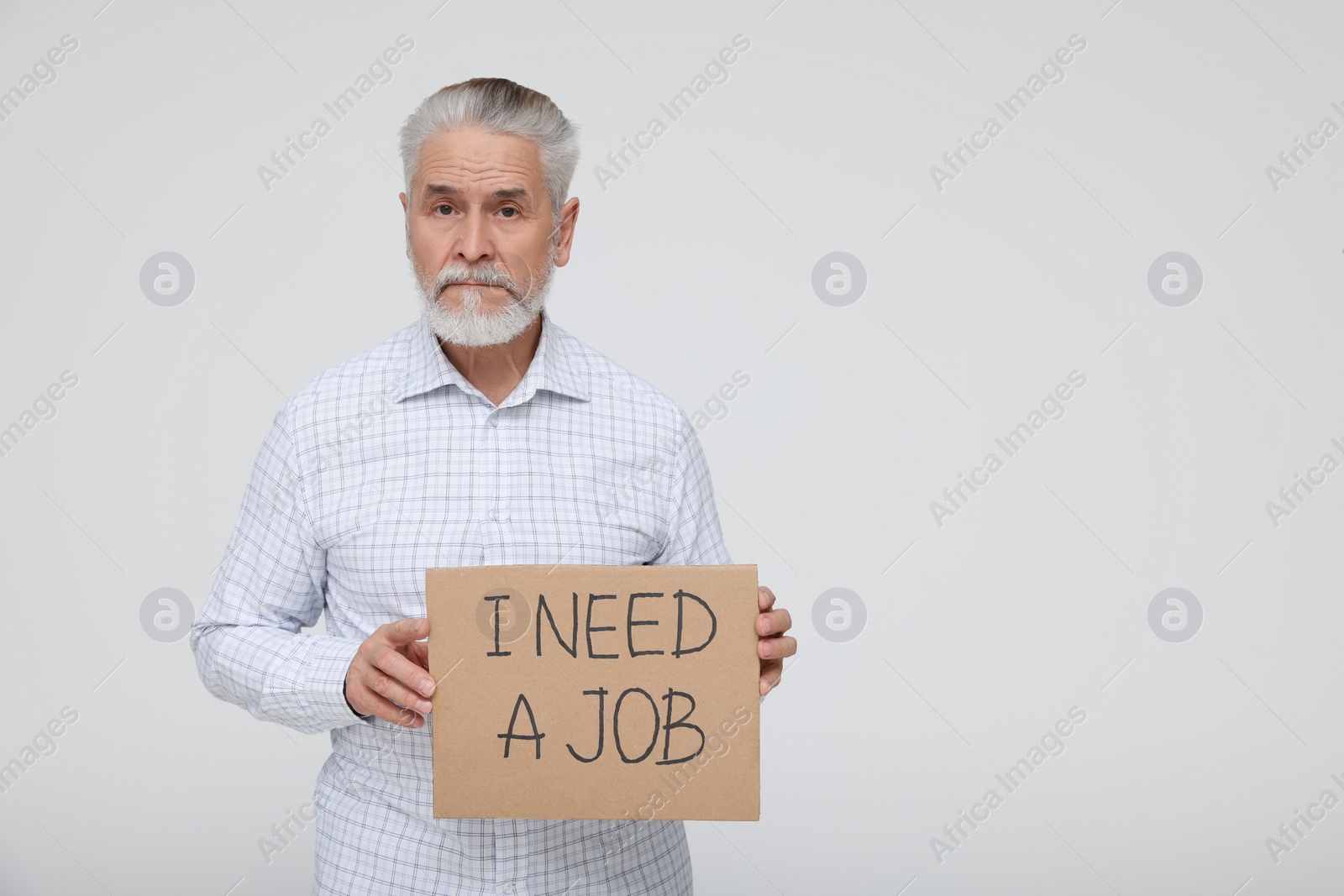 Photo of Unemployed senior man holding cardboard sign with phrase I Need A Job on white background. Space for text