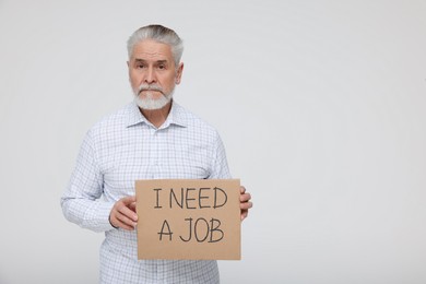 Photo of Unemployed senior man holding cardboard sign with phrase I Need A Job on white background. Space for text