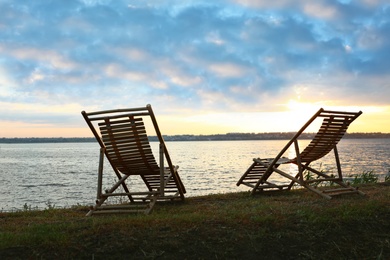 Photo of Empty wooden deckchairs on hill near calm river