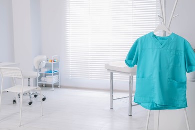 Turquoise medical uniform on rack in clinic. Space for text