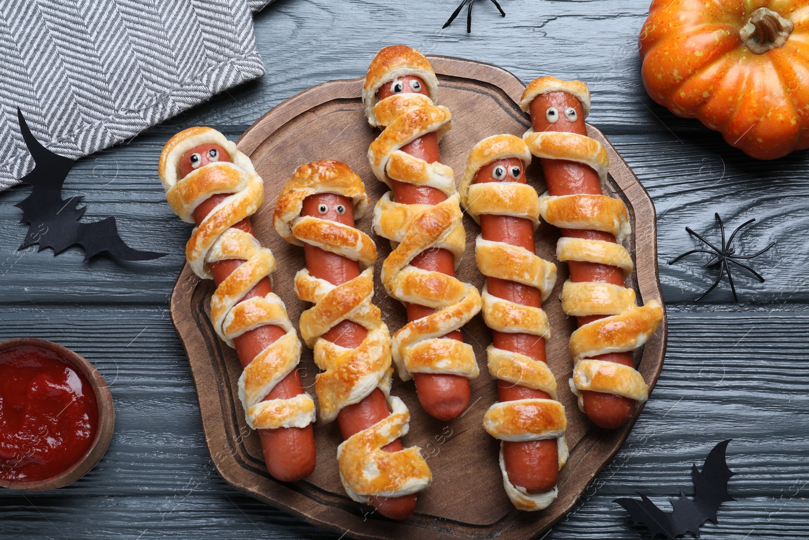 Photo of Cute sausage mummies served on wooden table, flat lay. Halloween party food