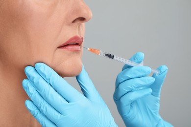 Photo of Doctor giving lips injection to senior woman on light grey background, closeup. Cosmetic surgery