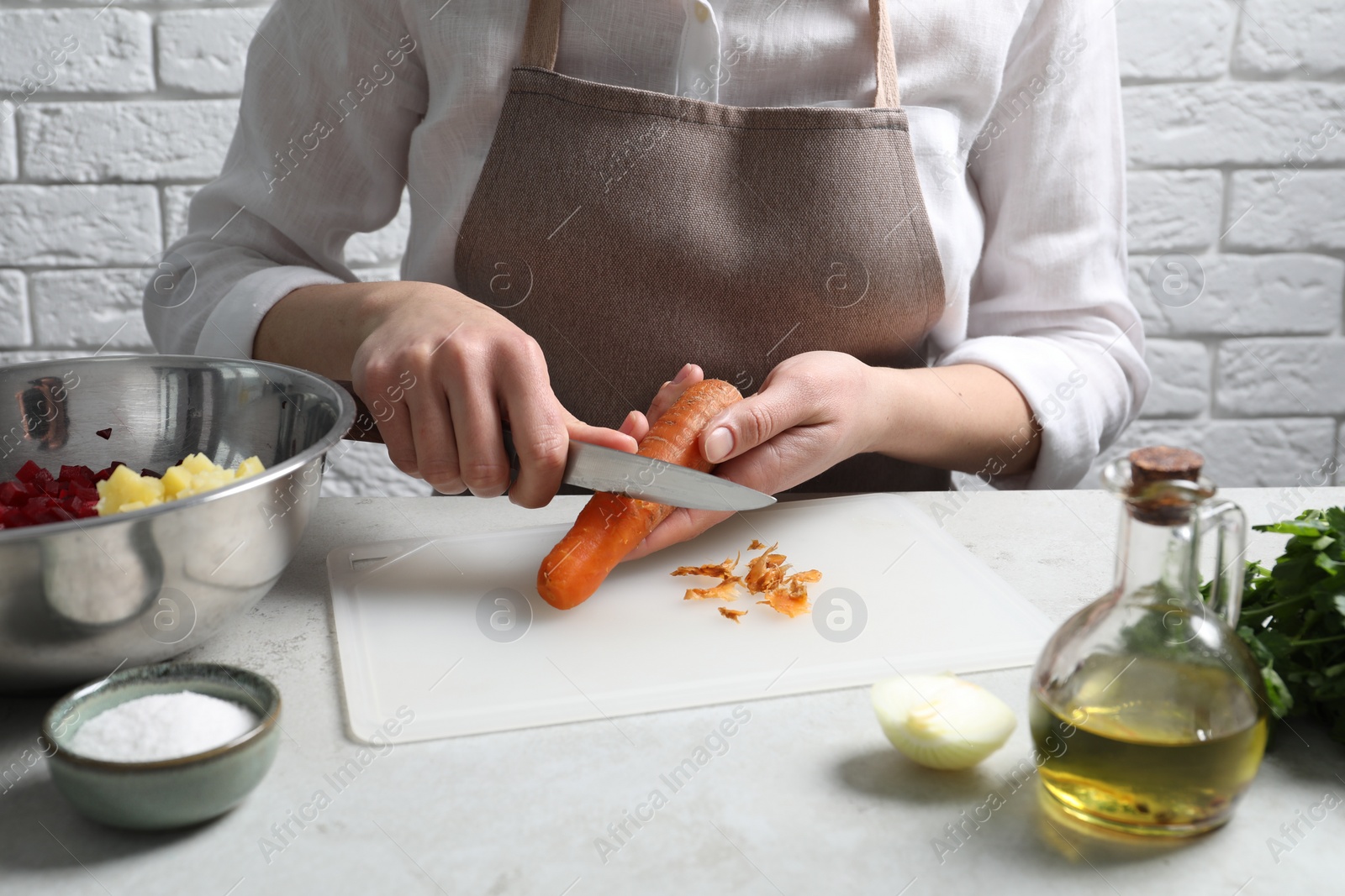 Photo of Woman peeling boiled carrot at white table, closeup. Cooking vinaigrette salad