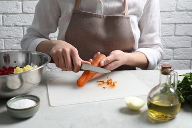 Woman peeling boiled carrot at white table, closeup. Cooking vinaigrette salad