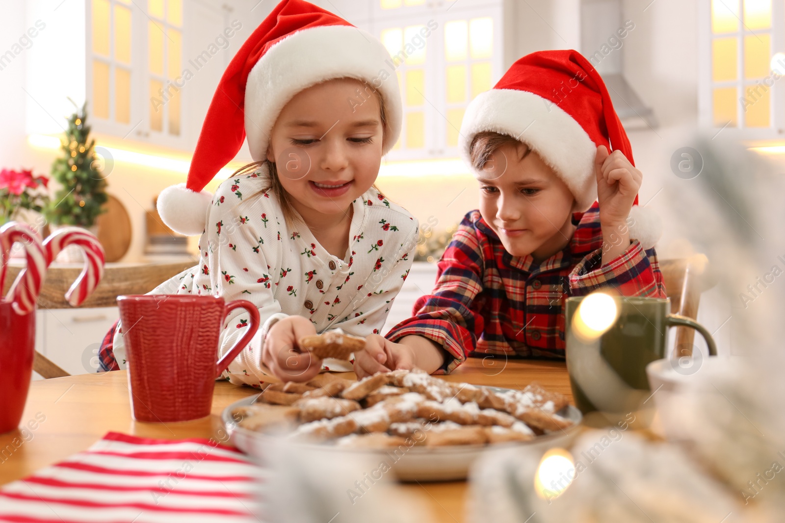 Photo of Cute little children taking tasty Christmas cookies from plate at  table in kitchen