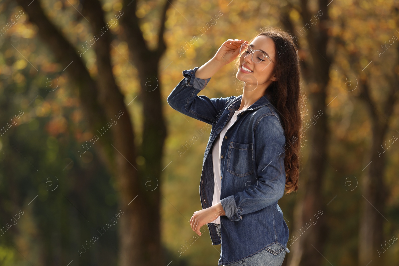 Photo of Young woman wearing eyeglasses in autumn park, space for text