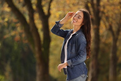 Young woman wearing eyeglasses in autumn park, space for text