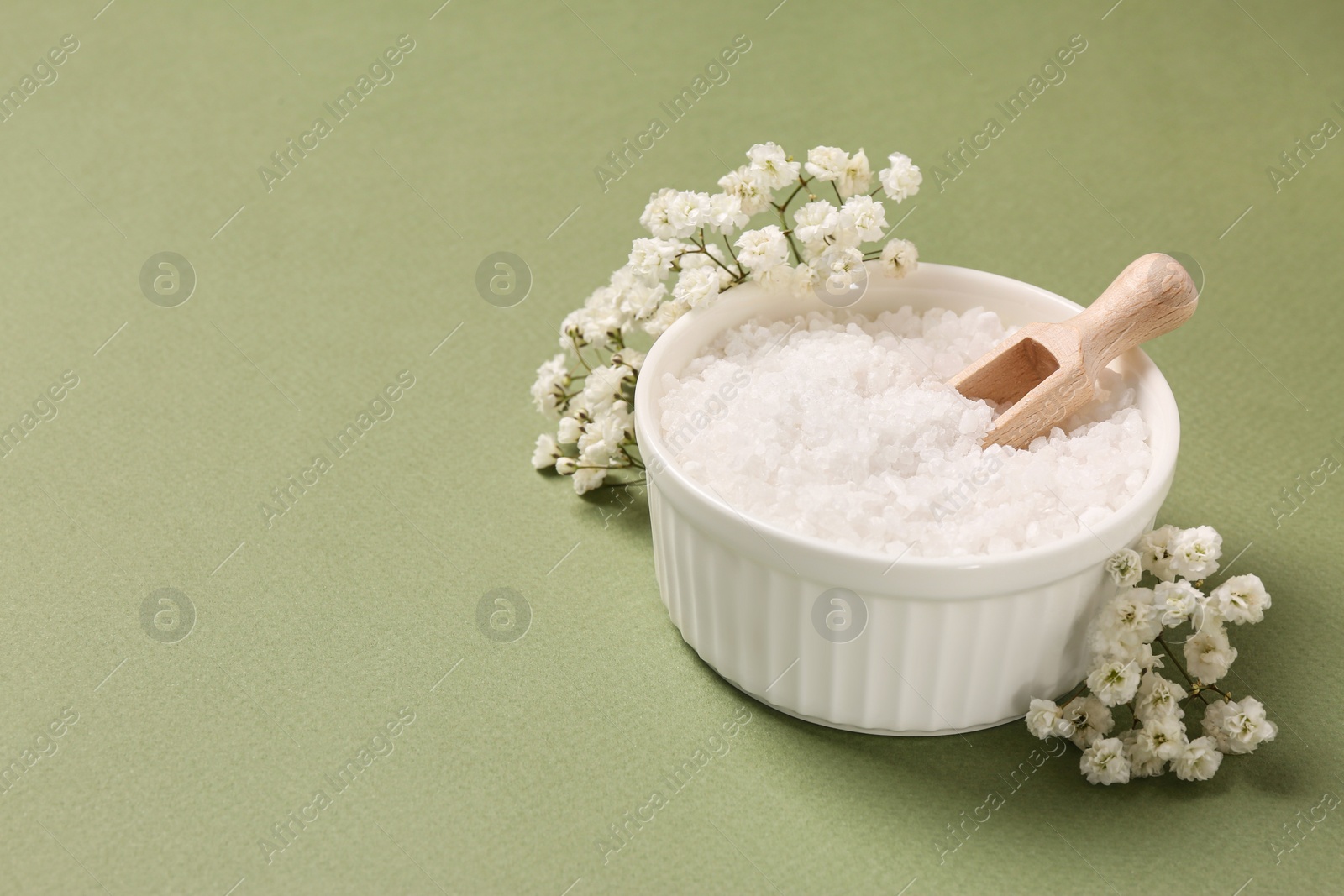 Photo of Bowl with sea salt and beautiful flowers on olive background. Space for text