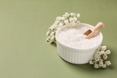 Bowl with sea salt and beautiful flowers on olive background. Space for text