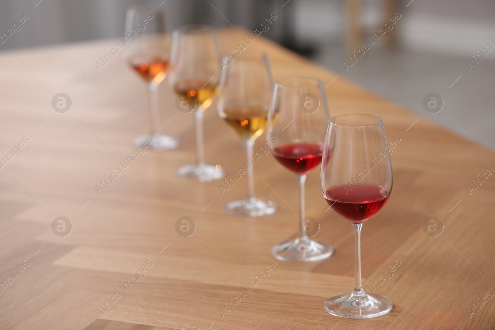 Photo of Different sorts of wine in glasses prepared for tasting on wooden table indoors