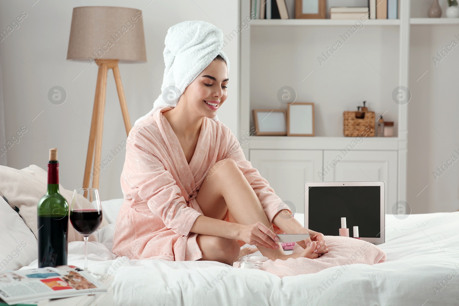 Photo of Beautiful young woman giving herself pedicure on bed at home