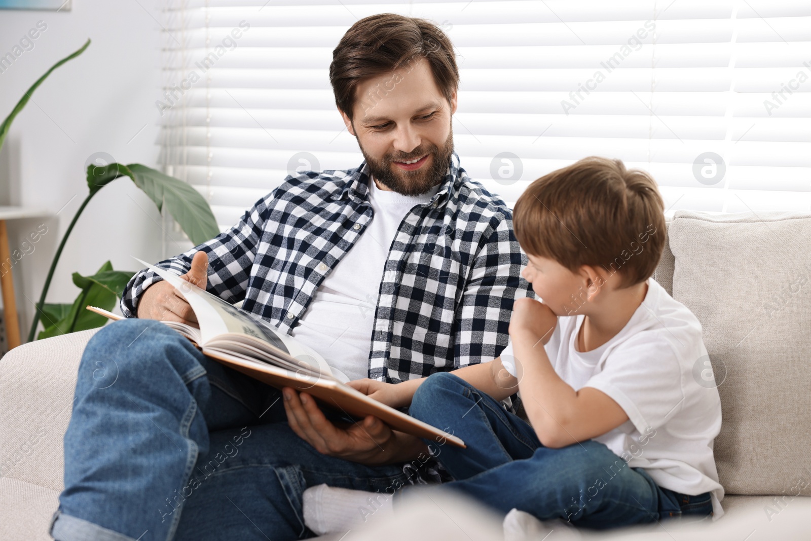 Photo of Happy dad and son reading book together on sofa at home