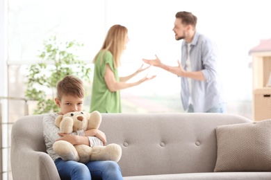 Photo of Little unhappy boy sitting on sofa while parents arguing at home