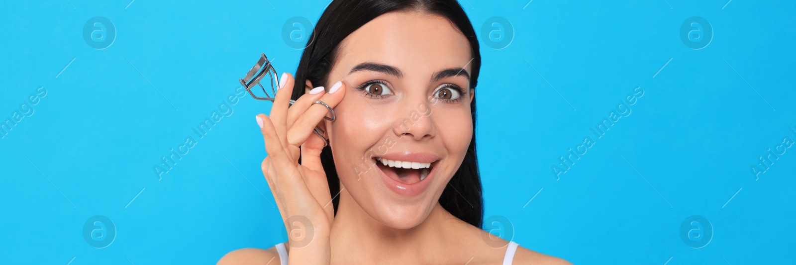 Image of Emotional young woman with eyelash curler on light blue background. Banner design