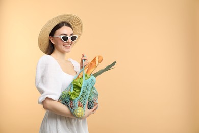 Photo of Woman with string bag of fresh vegetables and baguette on beige background, space for text