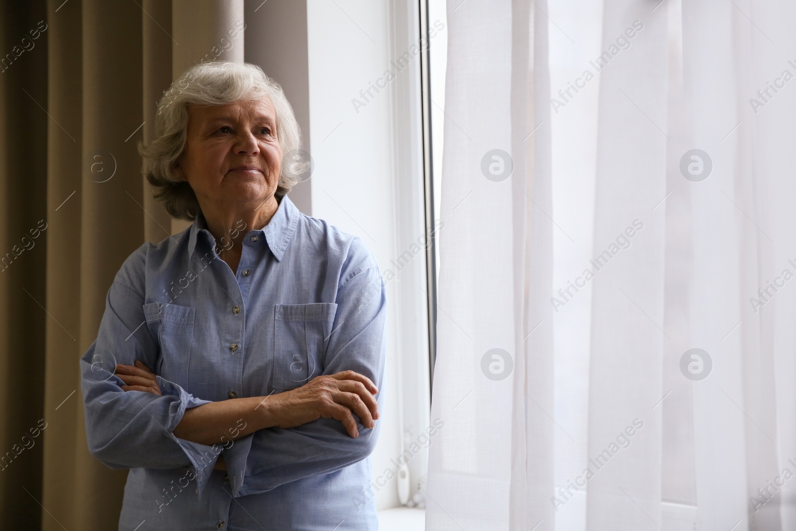 Photo of Portrait of elderly woman near window indoors. Space for text