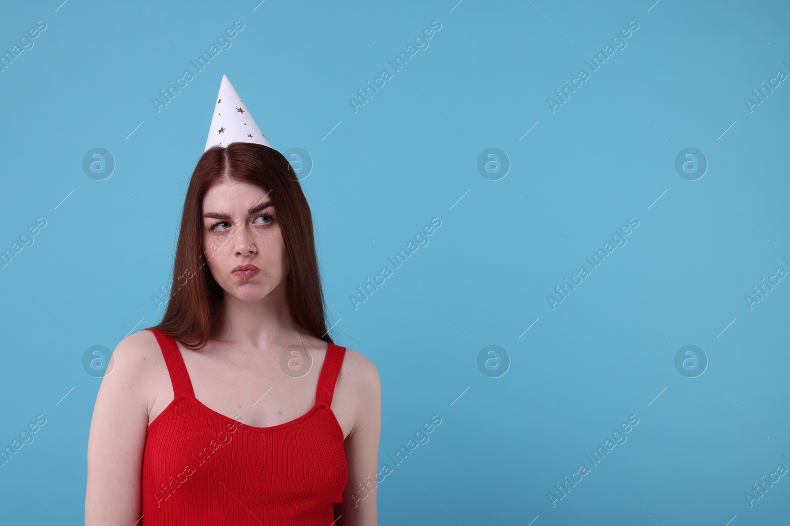 Photo of Sad woman in party hat on light blue background, space for text