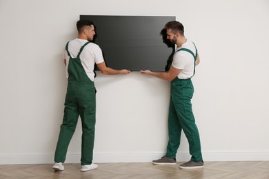 Professional technicians installing modern flat screen TV on wall indoors