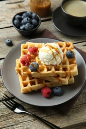 Photo of Delicious Belgian waffles with ice cream, berries and caramel sauce served on wooden table