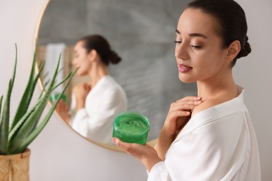 Young woman applying aloe gel onto her shoulder near mirror in bathroom