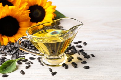 Photo of Sunflower cooking oil, seeds and yellow flowers on white wooden table