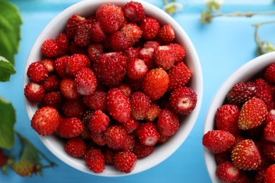 Photo of Fresh wild strawberries in bowls on light blue table, flat lay