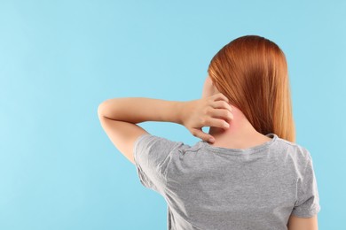 Photo of Suffering from allergy. Young woman scratching her neck on light blue background, back view. Space for text