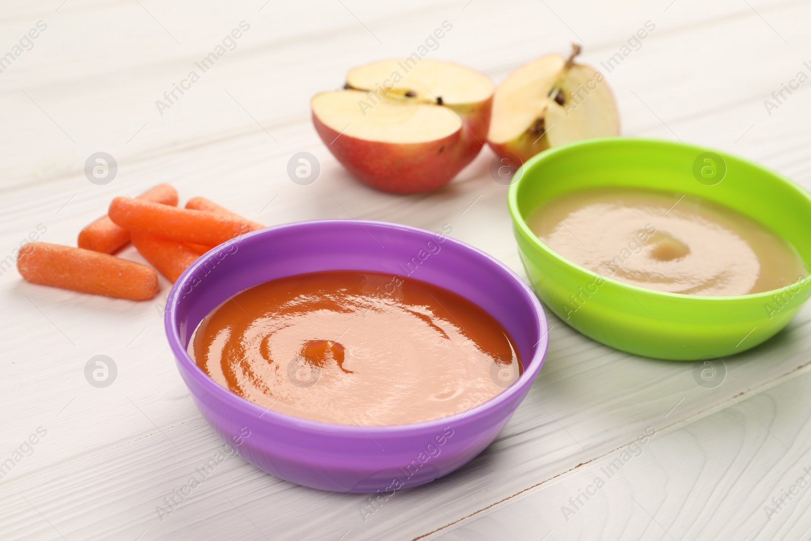 Photo of Baby food. Purees of apples and carrots in bowls on white wooden table