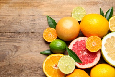 Photo of Different ripe citrus fruits with green leaves on wooden table, flat lay. Space for text