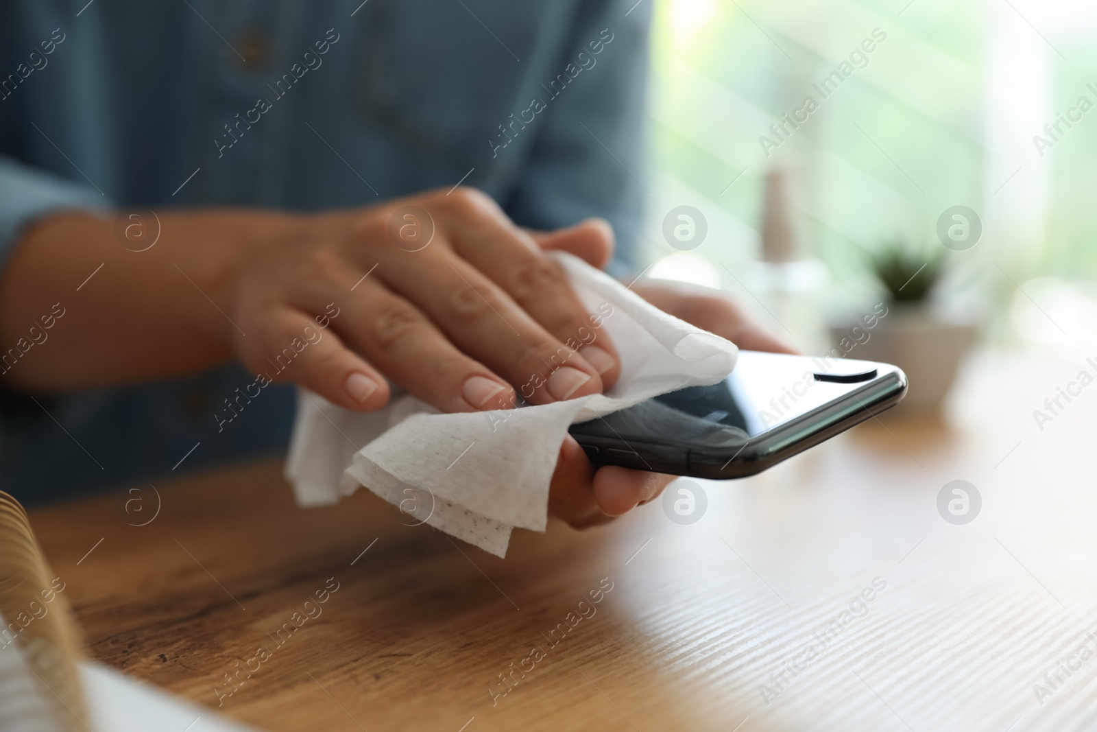 Photo of Woman cleaning smartphone with wet wipe at wooden table, closeup