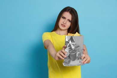 Photo of Unhappy young woman with bag of potato chips on light blue background