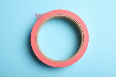 Photo of Roll of pink adhesive tape on light blue background, top view