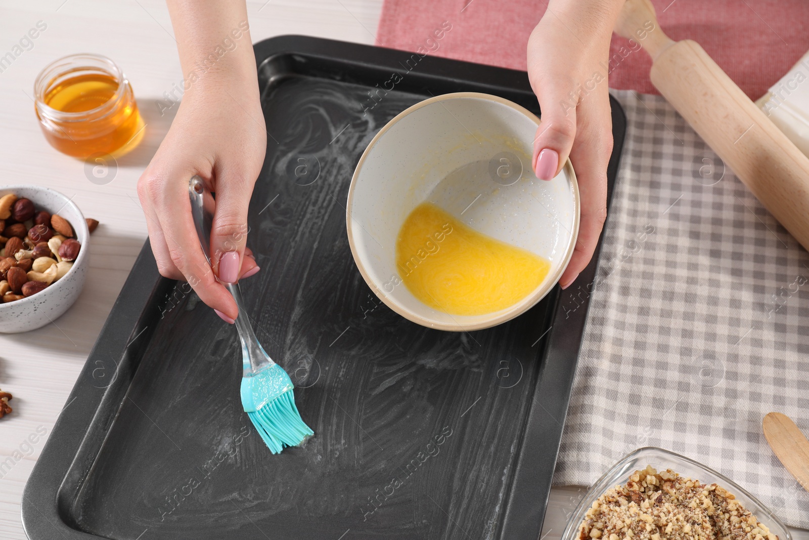 Photo of Making delicious baklava. Woman buttering baking pan at white wooden table, closeup