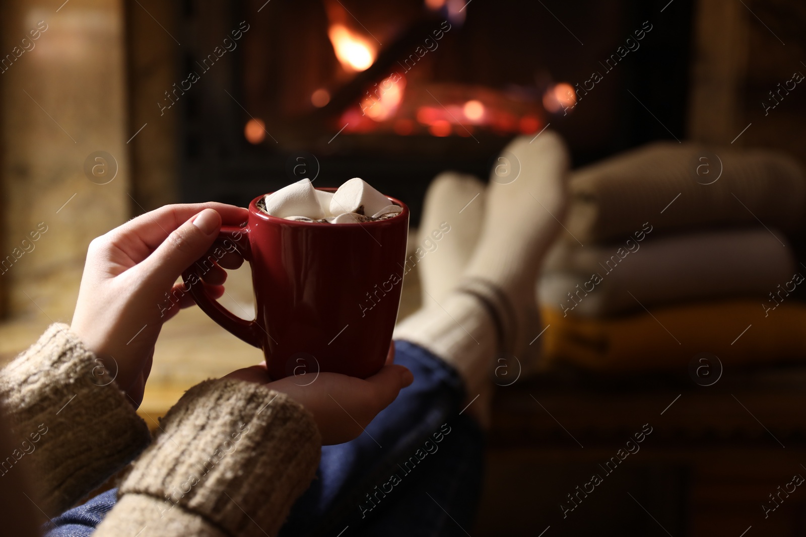Photo of Woman with cup of hot drink resting near fireplace indoors, closeup. Space for text