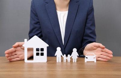 Photo of Woman with cutout paper family, house and car at table, closeup. Life insurance concept