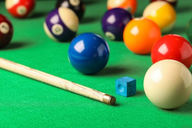 Photo of Many colorful billiard balls, cue and chalk on green table. Space for text