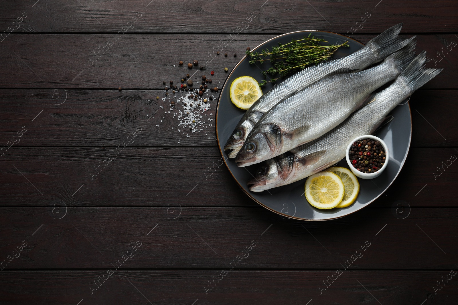 Photo of Tasty sea bass fish with spices on dark wooden table, flat lay. Space for text